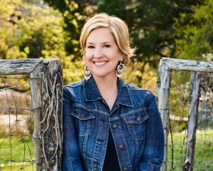 Brene Brown leaning on a rustic fence.