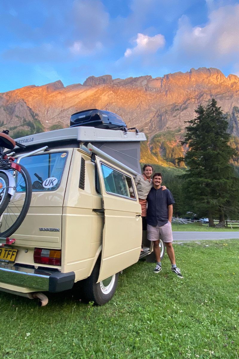 Katie and Abel with their yellow camper van with mountains in the background