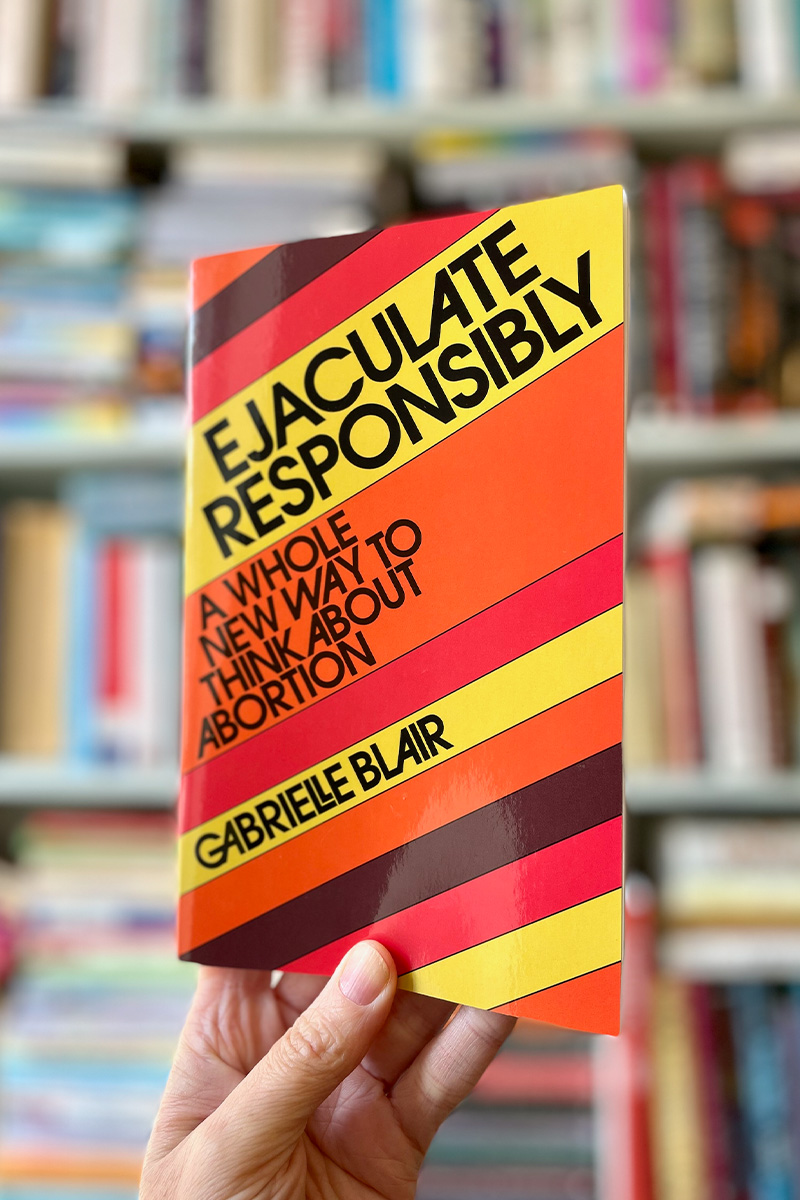 Photo of Gabrielle's book, Ejaculate Responsibly: A Whole New Way To Think About Abortion — an instant New York Times Bestseller, being held up in a library.