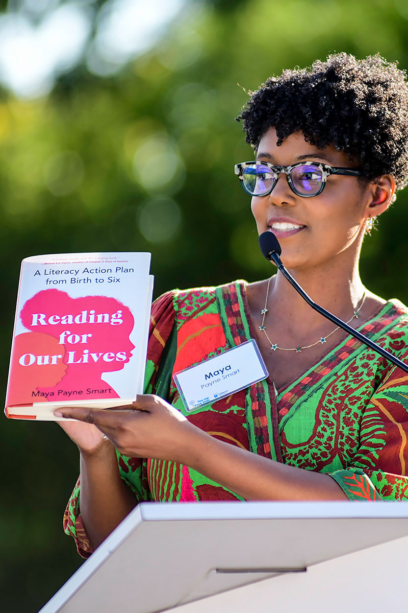 Maya speaks on a podium holding up her book “Reading for Our Lives.”