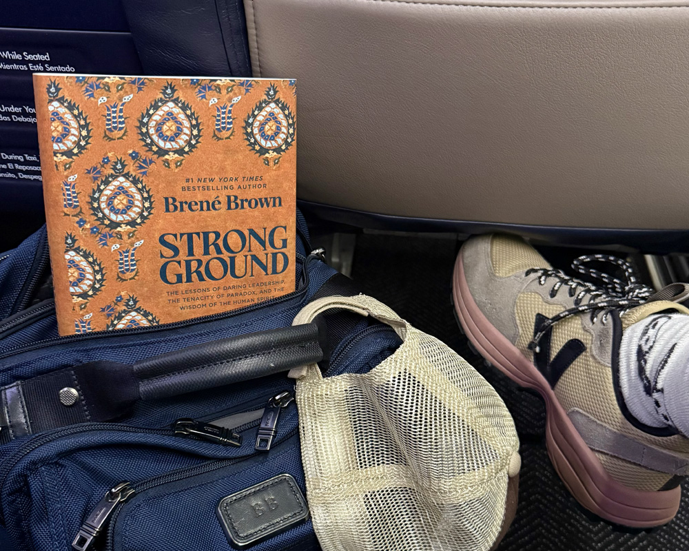 A copy of Strong Ground peeking out of a blue backpack on the floor of Brené’s airplane seat.