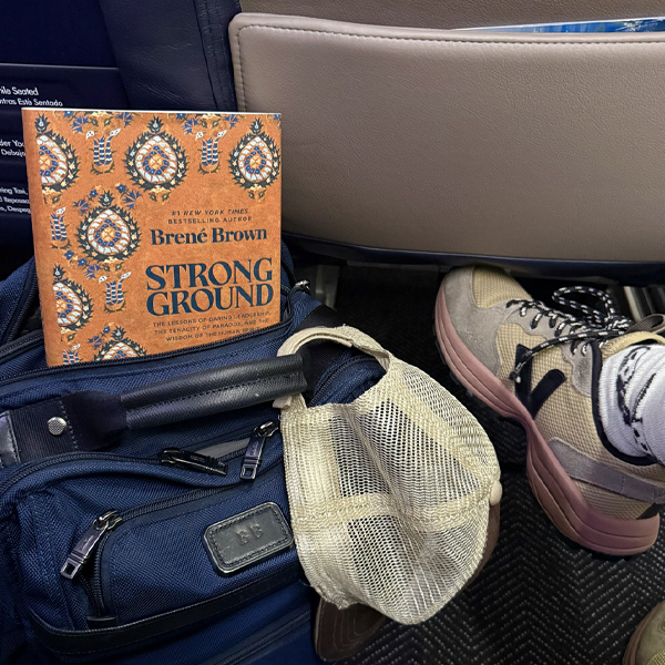 A copy of Strong Ground peeking out of a blue backpack on the floor of Brené’s airplane seat.