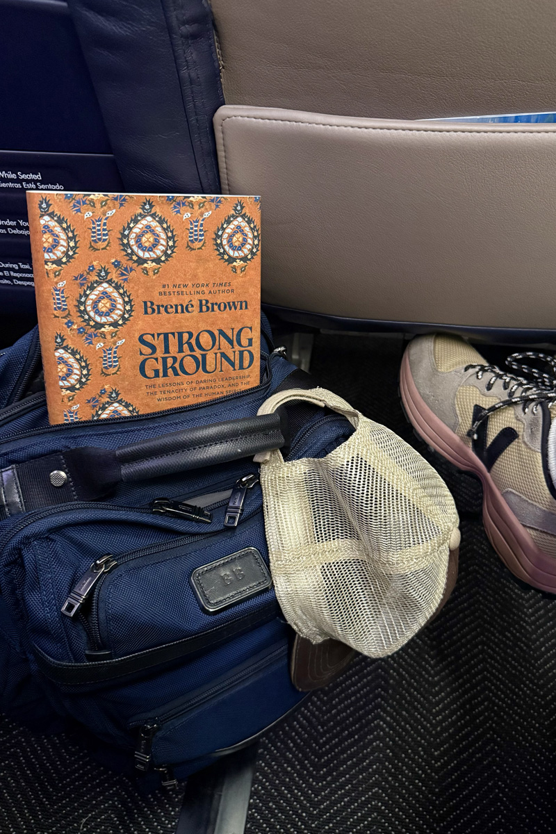 A copy of Strong Ground peeking out of a blue backpack on the floor of Brené’s airplane seat.