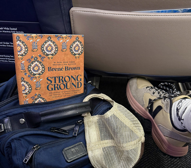A copy of Strong Ground peeking out of a blue backpack on the floor of Brené’s airplane seat.